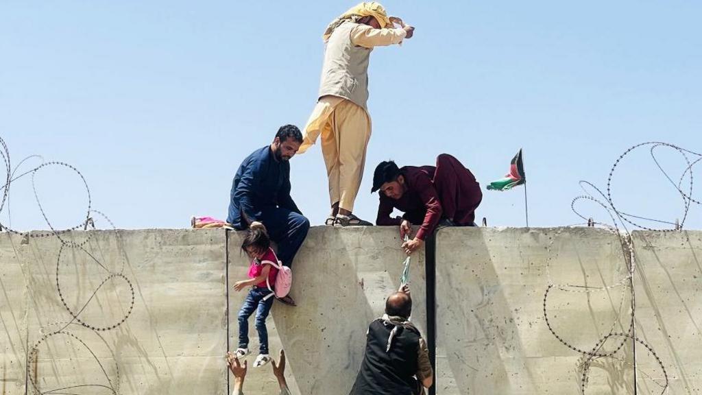Afghans scaling a wall to access Kabul airport during the evacuation in 2021