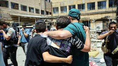 A health worker and other men walk in a hospital courtyard, past the bodies of victims of the recent clashes in Syria's southern city of Suweida on 17 July 2025