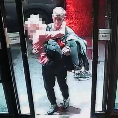 CCTV footage of Michael Harvey walking through hotel sliding doors carrying Carol O'Reilly in his arms. Her face has been blurred