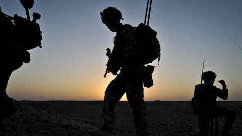 Silhouettes of British soldiers walking against a sunset in Afghanistan