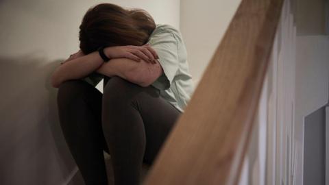 Woman sitting on the stairs with her head on her knees and arms over her head