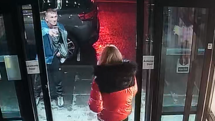 CCTV image of of Michael Harvey shouting at Carol O'Reilly at sliding doors of a a hotel. She is wearing a black and red jacket and he is wearing a blue jacket and is pointing at her