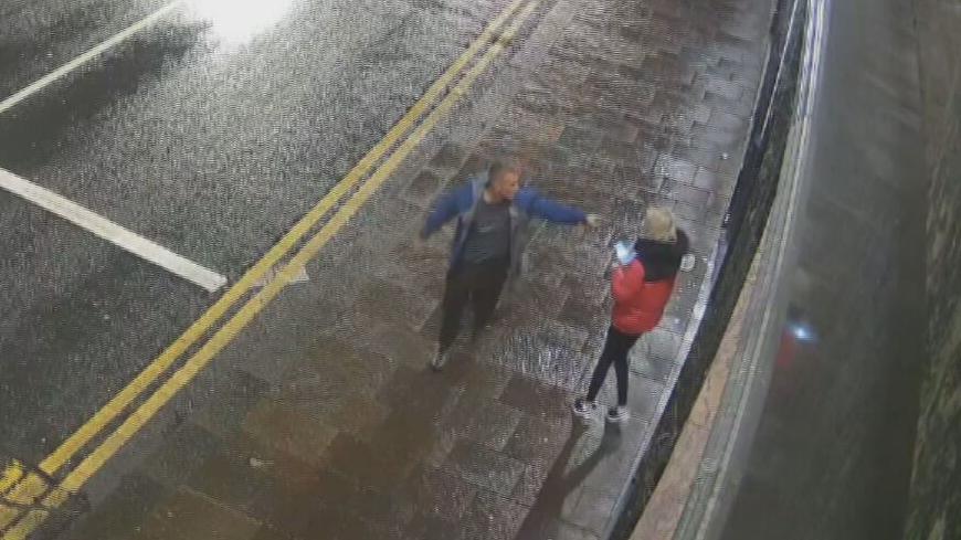 CCTV footage of Michael Harvey arguing with Carol O'Reilly on a street. He is pointing in her face, She is wearing a red and black jacket and he is wearing a blue jacket 
