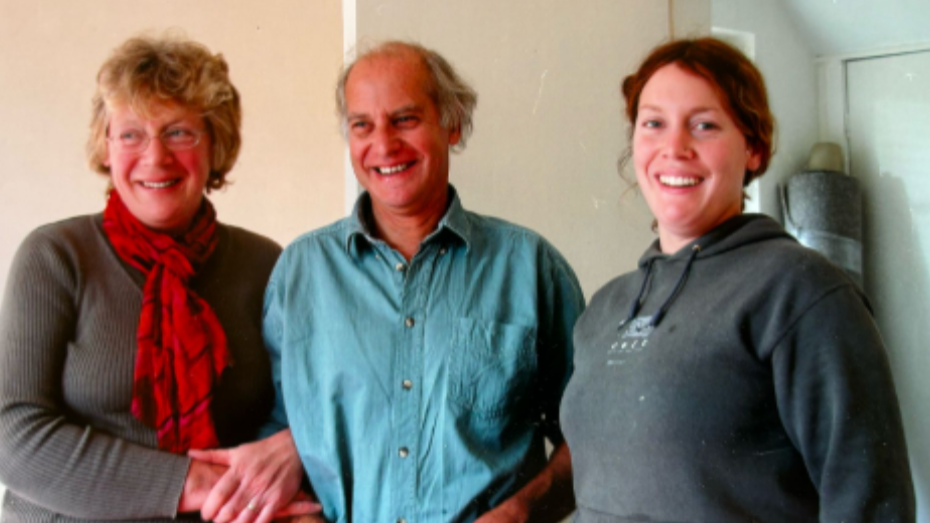 A family photo with Ros on the left, Martin in the middle and Debbie on the right. They are standing together with Ros and Martin arm in arm.
Ros is in a grey jumper with a red scarf, Martin is wearing a blue shirt and Debbie is wearing a grey jumper. All are smiling at the camera.