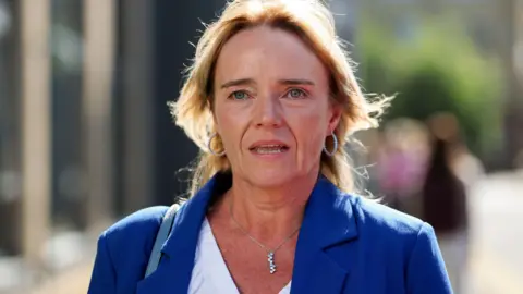 A woman with blonde hair in a blue jacket and white shirt. 